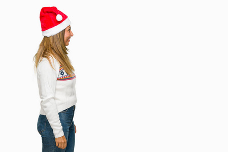 中年成年妇女穿着冬季毛衣和克莉丝马帽在孤立的背景寻找的一面, 放松轮廓姿势与自然的脸与自信的微笑