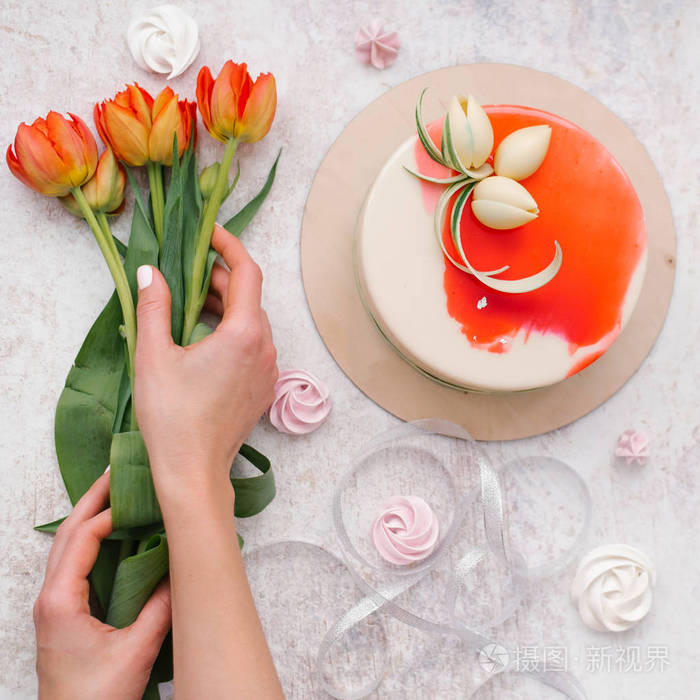 女性手捧红色郁金香, 白色和红色装饰蛋糕, 蛋白甜饼和丝带的食物构成