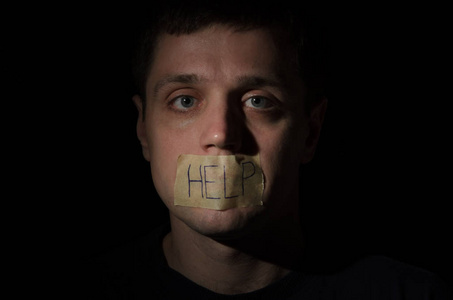 人质链在一条链子祈祷帮助与题字帮助在一个黑色背景上的嘴上的胶带上