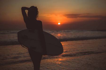 妇女手持冲浪板在海水中享受日落美景