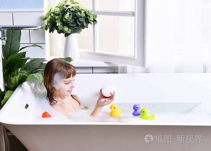 快乐的小女孩孩子坐在浴缸里的浴室