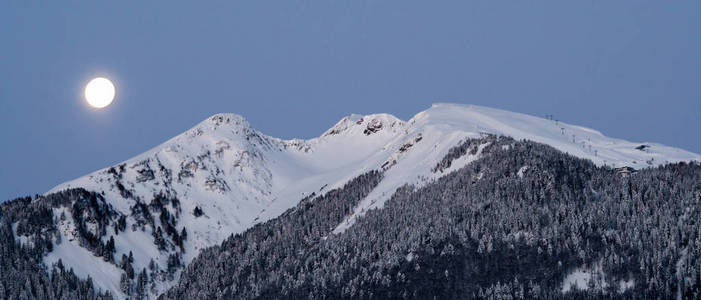 在瑞士阿尔卑斯山, 满月落在雪山后面, 森林和滑雪升降机在前景