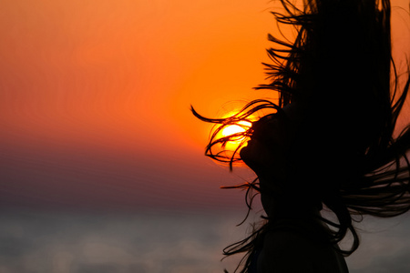 在日落时挥舞着头发的年轻女子的剪影