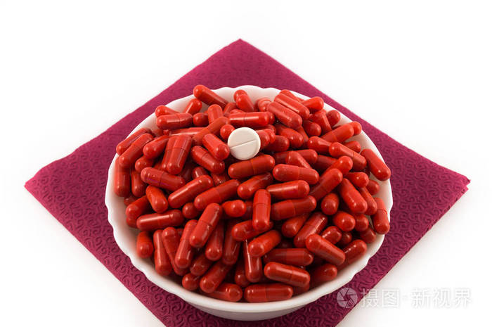 红色胶囊与医学在白色瓷杯子和一个白色圆的片剂在顶部