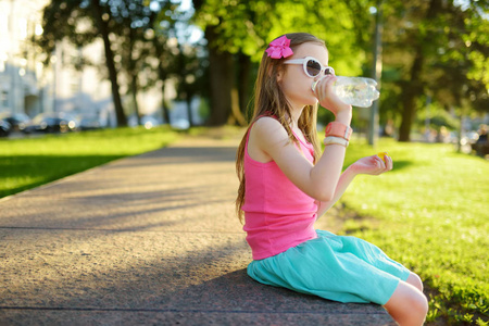 可爱的小女孩在炎热的夏日里喝水.孩子拿着一瓶水照片