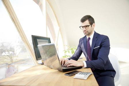 年轻的商人坐在他的笔记本电脑和键盘上打字, 而在线工作