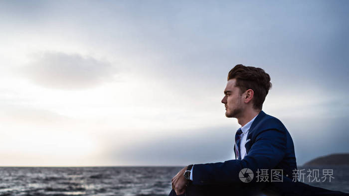 浪漫的优雅男人穿着西装坐在海天的背景上