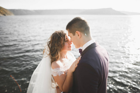 婚礼情侣接吻和拥抱蓝色海边的岩石上