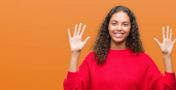 年轻的西班牙裔妇女穿着红色毛衣显示和指向手指十, 而微笑着自信和快乐