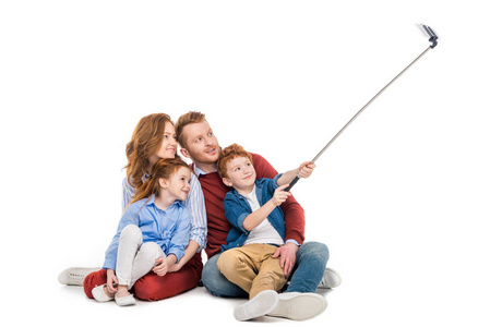 幸福的红头发的家庭坐在一起, 并采取自拍与智能手机隔离白色