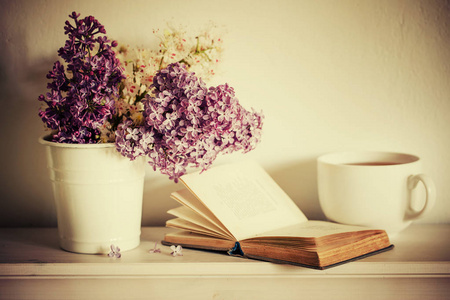 紫色丁香与开放的书和白杯茶