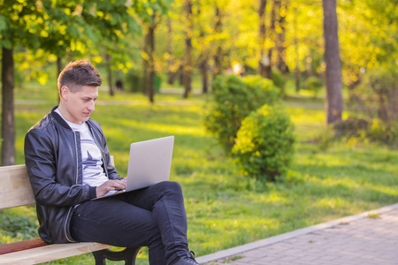 一个年轻英俊的男人坐在公园里用笔记本电脑工作。那个自由职业者在外面工作