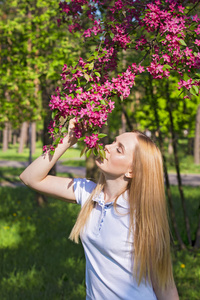 美丽的金发女人闻到苹果树的花朵。女孩和盛开的苹果树。春天与树花的时间