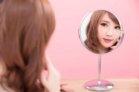 美丽的女人微笑着看着镜子上的粉红色背景