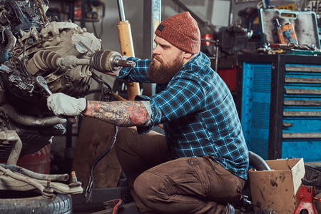 一个野蛮的纹身长胡子的机械专家修理汽车发动机, 这是在液压升降机在车库上提出。服务站