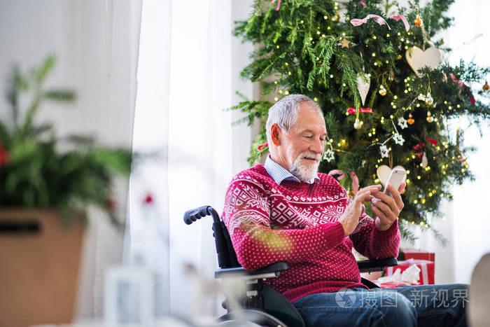 一个坐在轮椅上的老人在圣诞节时在家中使用手机, 发短信