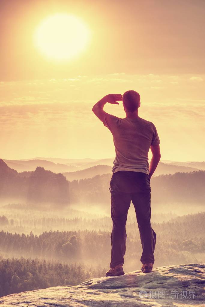 男性徒步者站在边缘享受着朦胧的风景的戏剧性俯瞰太阳藏在浓雾中改变