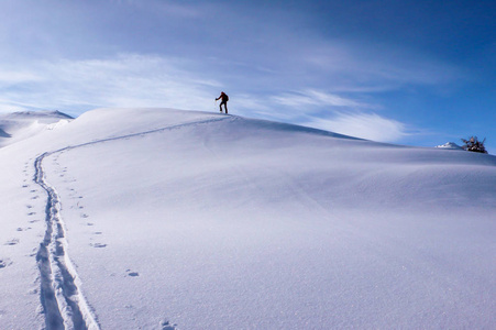 一只雄性野外滑雪者徒步上山, 爬上一座长山山脊, 朝向瑞士阿尔卑斯山克洛斯特斯附近的山顶上过冬。