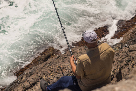 在暴风雨中, 渔夫站在岩石上钓鱼竿