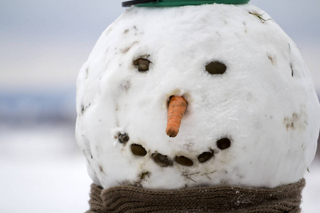 特写大搞笑原始笑雪人头与胡萝卜鼻, 黑石眼睛和牙齿在儿童围巾上光模糊复制空间户外背景。圣诞快乐, 新年愉快。