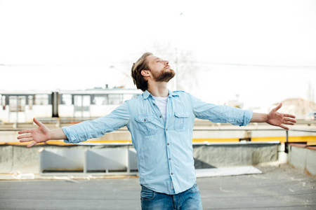 站在外面的蓝色衬衫, 微笑着, 有一个积极的态度, 张开双臂仰望天空