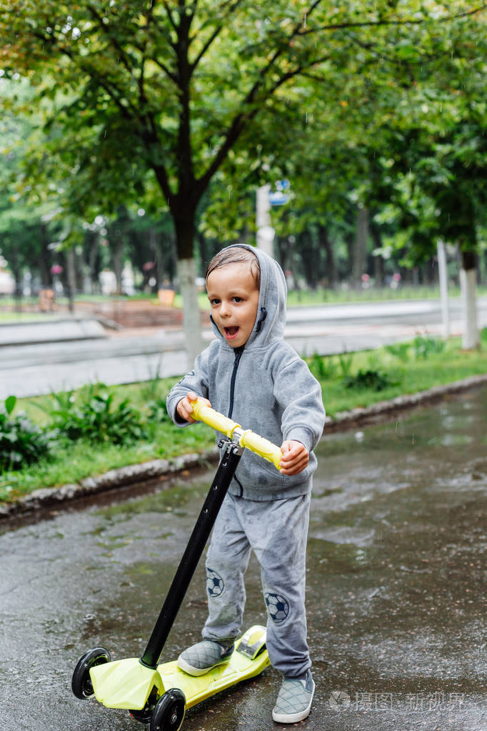 湿透在雨中一个男孩穿着运动西装溜冰鞋春季漫步在城市公园阴雨天气