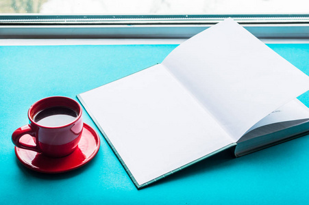 一杯咖啡和一本蓝色背景的书在窗边。概念早在家里。样机