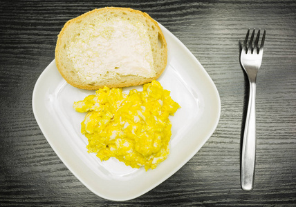 炒鸡蛋和一块面包, 黄油放在白色盘子上。从上面查看