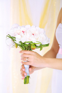 新娘紧握着的白牡丹的婚礼花束特写时，在明亮的背景上
