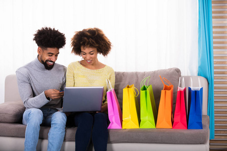 年轻夫妇网上购物在沙发上多彩色购物袋