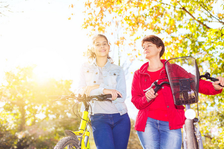 在秋季公园的母亲和女儿骑自行车
