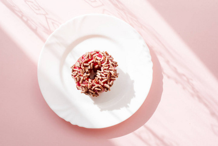 甜甜圈覆盖红釉, 并洒在粉红色背景下的白色板上的磨碎巧克力与表面图案的阴影