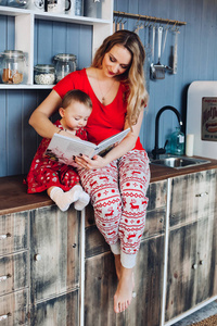 美丽的母亲与小女儿在圣诞节睡衣阅读书在厨房