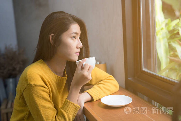 亚洲妇女在早晨的窗口角落里放松和喝咖啡