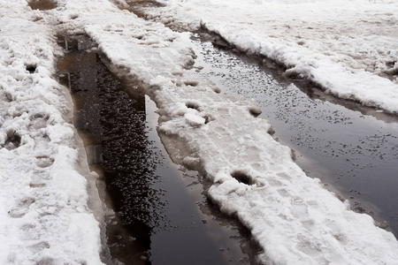 在城市街道上的巨大的雪坑特写.道路上积雪和冰的影子.春季洪水照片