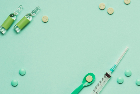 在绿色背景的药物, 药丸和注射器的安瓿的顶部视图照片