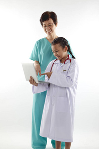 在医生服装聊天的老妇女和女孩, 同时拿着在白色背景隔离的笔记本电脑