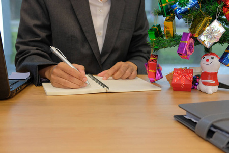 在笔记本上写提醒计划笔记的人。在圣诞新年假期工作办公室的生意人工作组织计划