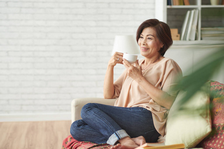 坐在沙发上喝杯茶的亚洲女人的肖像