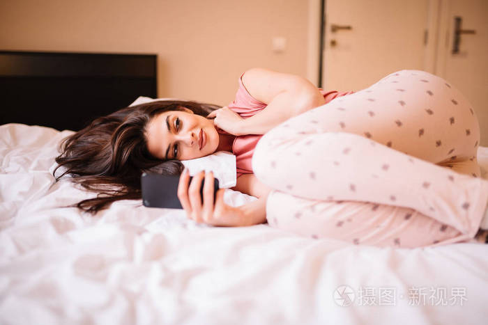 漂亮的女孩躺在床上采取自拍或视频聊天或思考她的男朋友