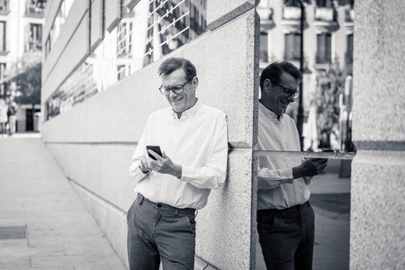 英俊快乐的人在他的60s 发送和接收短信在他的手机在老人使用社交网络现代技术保持联系和企业家创意业务概念