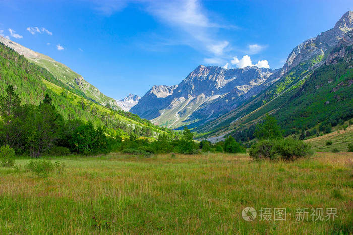 山峡谷与草甸在早晨在绿色草和花围拢由山峰在夏天