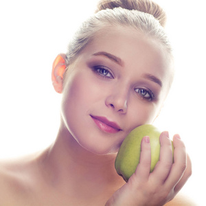 特写肖像一个美丽的金发女孩与化妆举行绿色苹果旁边的她的脸颊对白色背景