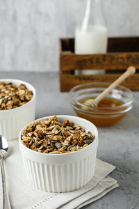 用一瓶牛奶和蜂蜜在亚麻餐巾上的白色碗里自制的麦片。健康早餐的食物摄影