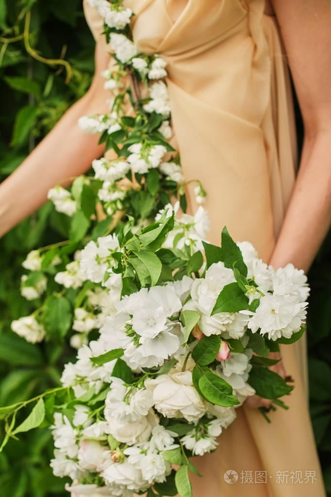 穿着浪漫粉色连衣裙的女孩捧着一束白色玫瑰站在户外绿色背景柔和柔和
