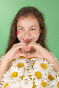 一个年轻女孩的肖像与一束 chamomiles 和心脏的象征脸上。在绿色背景上隔离