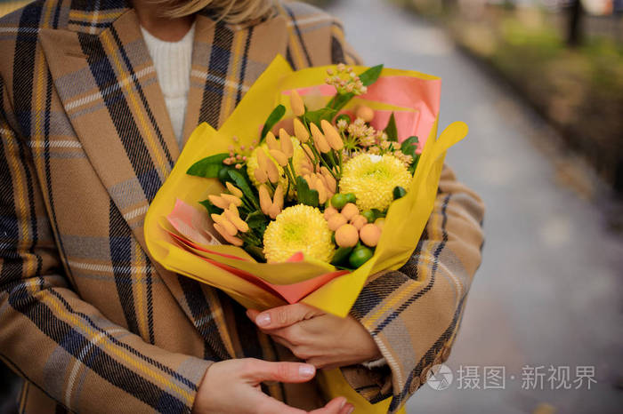穿着格子大衣的女人在寒冷的秋日捧着一束鲜艳的黄色花朵.