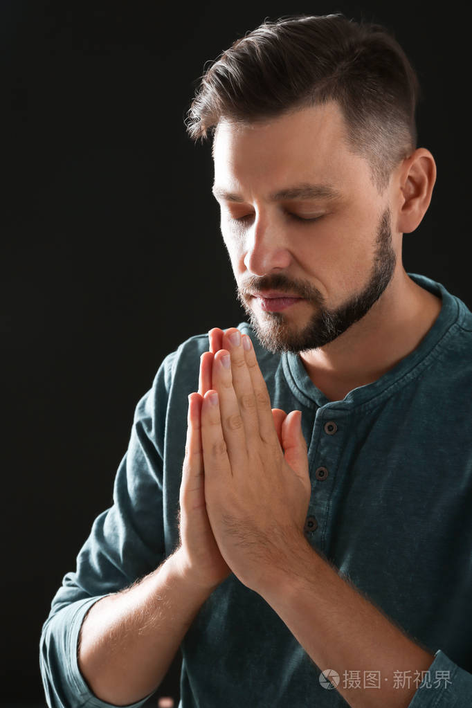 双手紧握在黑色背景上祈祷的男子