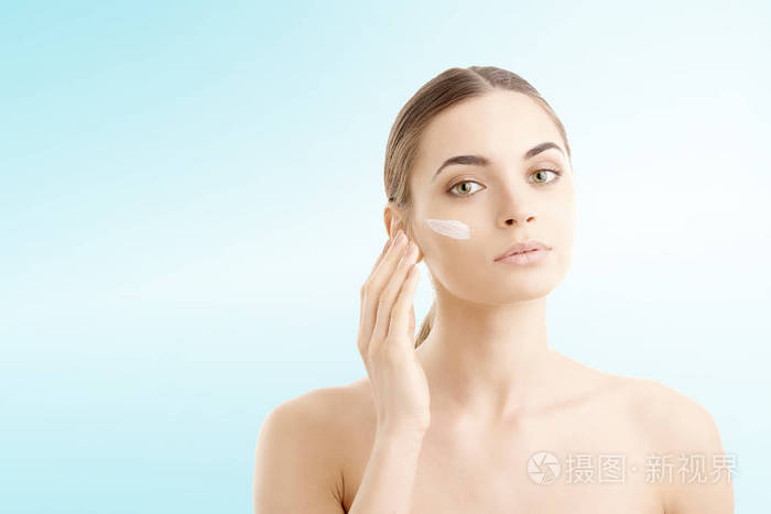 工作室拍摄一个美丽的年轻女子涂抹在她的脸上的润肤霜与复制空间的