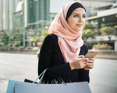带有购物袋和手持手机的伊斯兰妇女